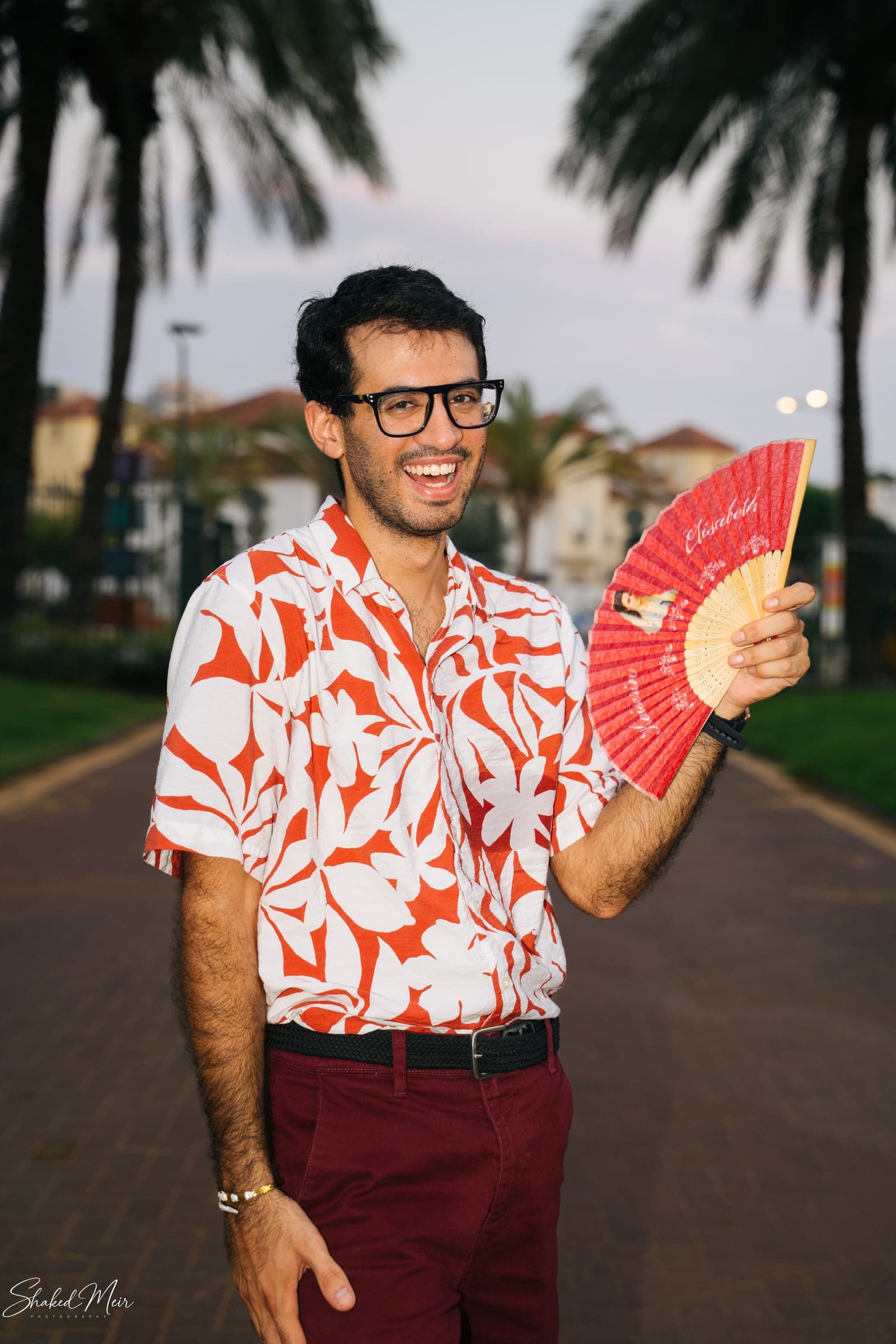 גבר בחולצה פרחונית עם מניפה ליד עצי דקל