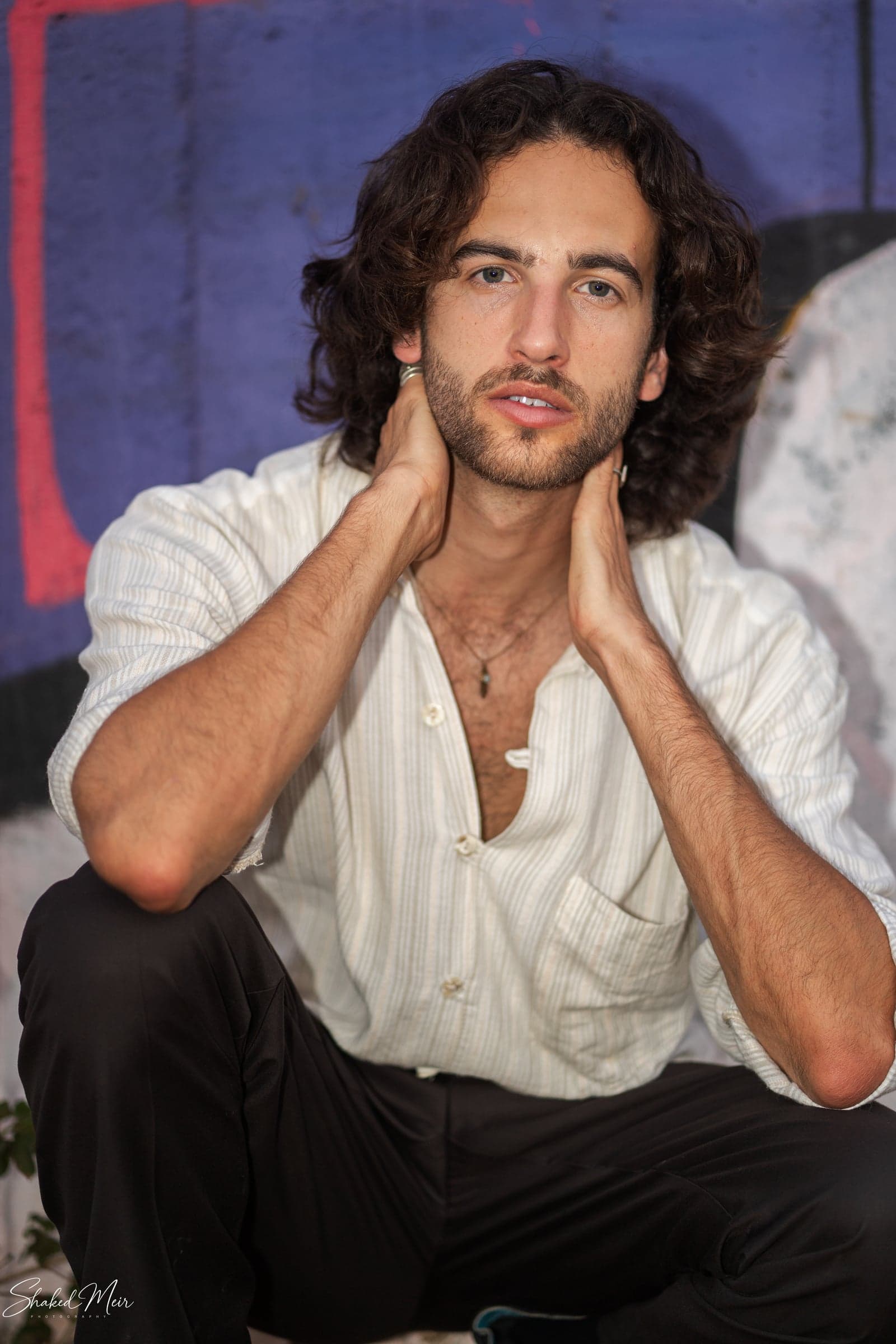 פורטרט ישיבה של גבר בחולצה לבנה על רקע צבעוני